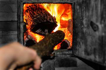 Open firebox with burning firewood. A man's hand is laying wood inside the furnace