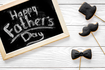 Naklejka premium Words happy Father's day written on blackboard. Black tie, mustache and hat cookies. White wooden background top view