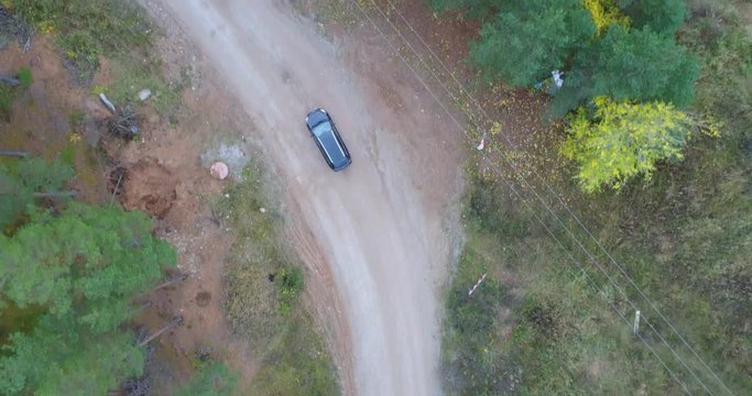 Aerial view of the car driving among the green pine forest. Autumn landscape. Amazing aerial perspective of car amon the woods. Tall pine trees in forest. Autumn trees.