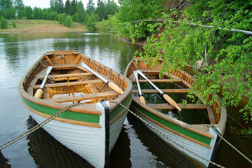 Two small rowing boats are moored in a quiet bay by a overgrown shore.
