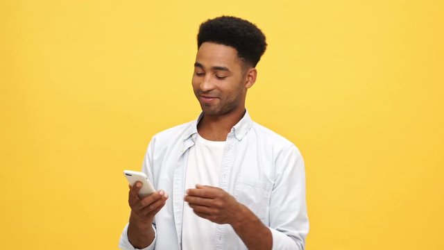 Young african man in shirt choosing between a book and smartphone and stops on the phone over yellow background