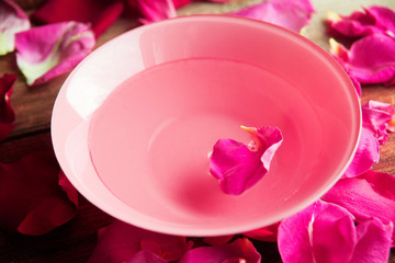 Pink and white rose petals in silver bowl with water on wooden background