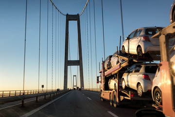 Brand-new cars on a car transport truck. Car transporter trailer on the long bridge in the evening