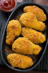 Close-up of chicken wings with breading and sauce served in a metal plate, selective focus