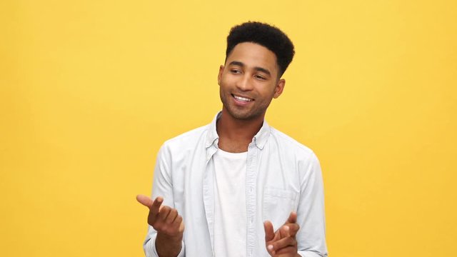 Happy african man in shirt recounts something on his fingers and looking at the camera after that over yellow background
