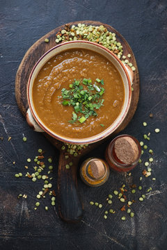 Bowl of cream-soup with peas and curry on a rustic wooden serving board, flat-lay on a scratched dark brown metal surface