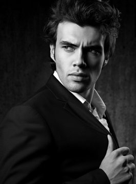 Confident ambitious handsome man with strained look posing in fashion suit and white style shirt on dark shadow background. Closeup black and white portrait