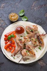 Tortillas with barbecued chicken wings on skewers and vegetables, studio shot
