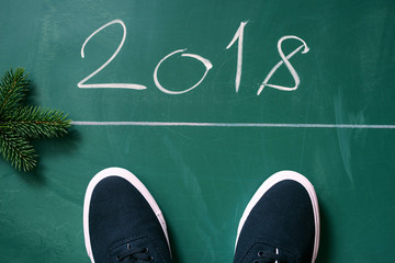Text chalk 2018 and black sneakers from above on a green blackboard. Conceptual congratulation happy New Year