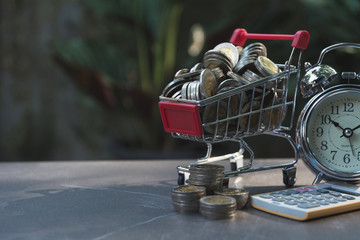 Coins in shopping cart with money stack step growing money and alarm clock. Concept finance business and shopping investment.