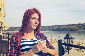 Fototapeta na wymiar Thoughtful redhead woman enjoying in cup of coffee.