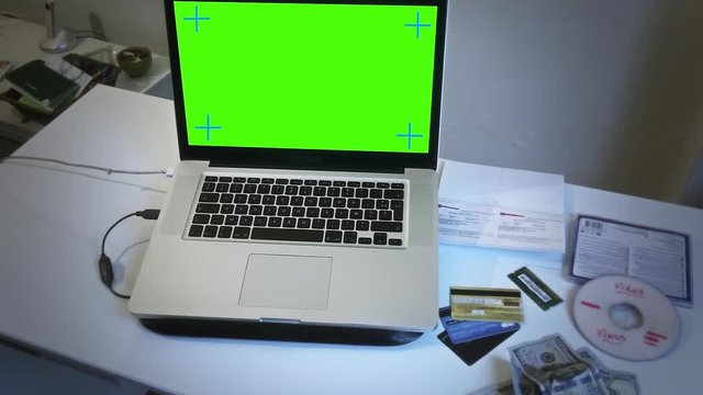Hacker Crime Scene With Green Screen Computer, Pan Movement. Green screen laptop next to stolen credit cards, dollar bills and virus dvd simulating a hacker crime scene