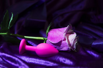 Silicone dildo Sex toy and a pink rose on a dark background.