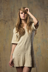 Fototapeta premium A beautiful young model is posing in short stylish beige dress. An image in beige tones. Abstract background. 