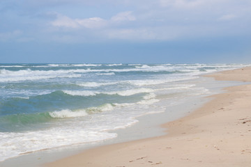 Sea coast waves rolling on sandy beach, stormy cloudy sunrise