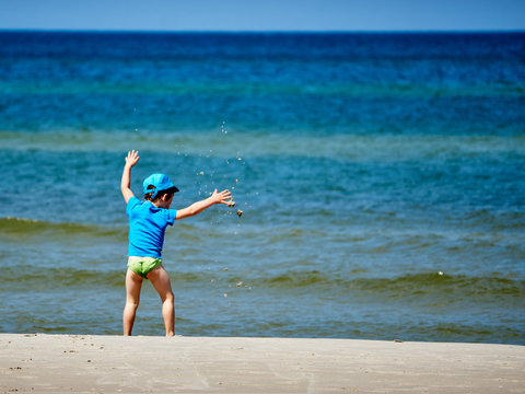 Mały chłopczyk rzuca zabawnie piaskiem na plaży nad morzem.