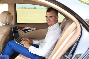 Young businessman using laptop in a car