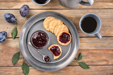 Tray with bowl of plum jam and cookies on wooden table