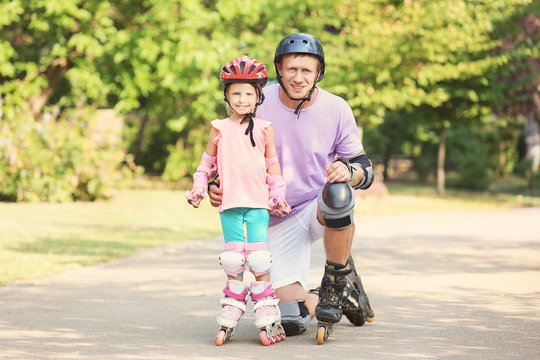 Father with daughter on roller skates in summer park