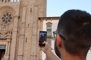 A young man taking a picture of a catherdal with a cellphone
