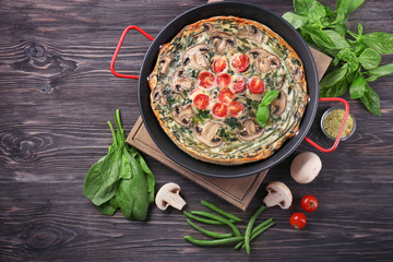 Frying pan with delicious spinach frittata on wooden background