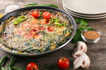 Frying pan with delicious spinach frittata on table