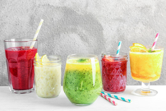 Glasses with different smoothies on table against color background