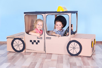Little children playing with cardboard taxi in light room