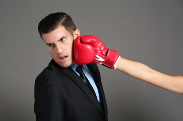 Hand of woman in boxing glove hitting businessman on grey background