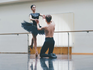 Young man practicing in classical ballet with young beautiful woman in black tutu clothing in the gym. Minimalism interior, dancing sensual dance. © kohanova1991