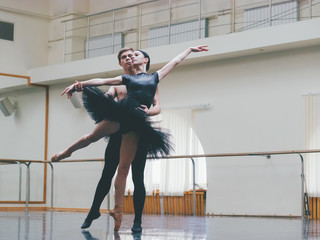 Young man practicing in classical ballet with young beautiful woman in black tutu clothing in the...