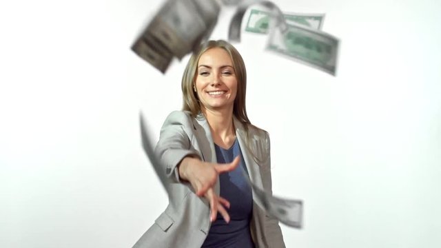 Slowmo of smiling businesswoman standing against studio backdrop and throwing wad of dollar bills at camera