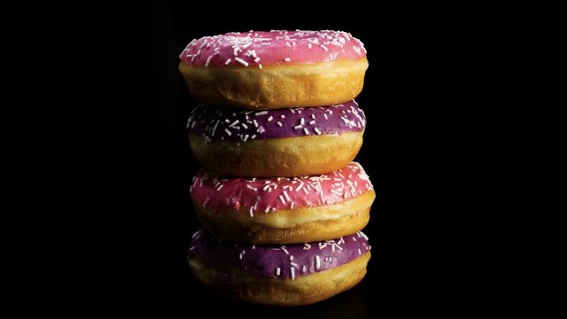 Freshly baked donuts stacked on each other rotate against black background