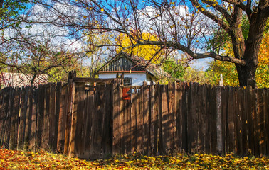 Old small white house in the style of ancient Ukrainian traditions seen behind a tall old wooden fence