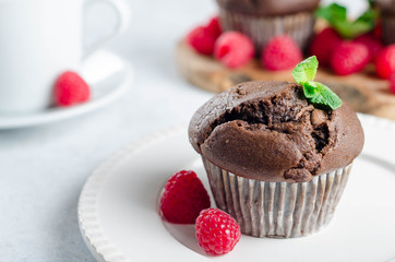 One chocolate muffin on a foreground and two muffins on a wooden board with fresh raspberries on the background, copy space for your text