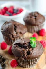 Three chocolate muffins on a wooden board with fresh raspberries, vertical image