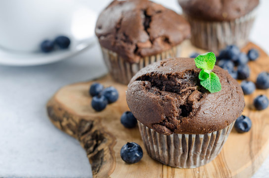 Three chocolate muffins on a wooden board with fresh blueberries, horizontal image