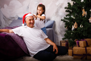 Obraz premium Picture of an elderly man wearing a Santa hat while playing with his grandchildren near a Christmas tree