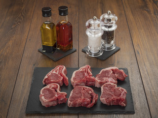 Raw lamb chops on a stone board, salt, pepper, diffused oils in the background,