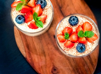 Homemade italian dessert tiramisu with strawberries, mint and blueberry in glass top view