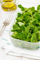 Fresh raw salad leaves in plastic box on  light wooden background. Selective focus.