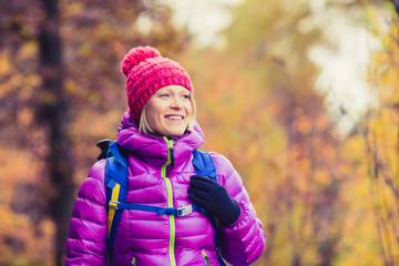Hiking woman with backpack looking at camera in inspirational autumn golden woods