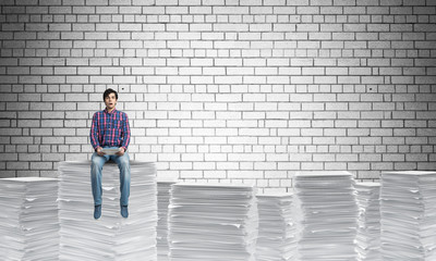 Attractive man sitting on pile of paper documents.