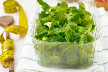 Fresh raw salad leaves in plastic box on  light wooden background. Selective focus.