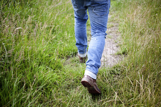 Photo of a man's legs walking on a small path with grass on both sides