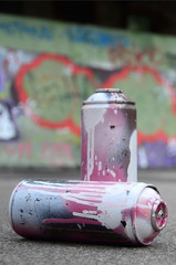 A few used spray cans with pink and white paint lie on the asphalt against the background of a...
