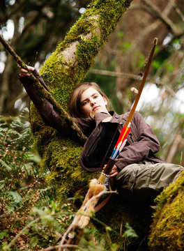 A young girl relaxing in tree holding bow and arrow.