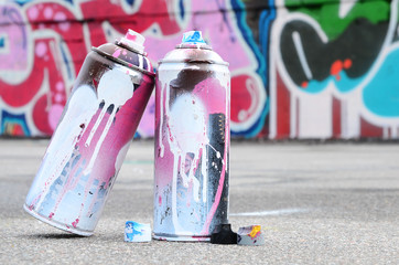 Several used spray cans with pink and white paint and caps for spraying paint under pressure is...