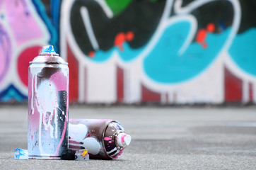 Several used spray cans with pink and white paint and caps for spraying paint under pressure is...