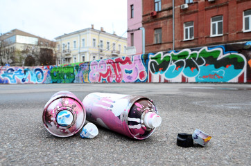 Several used spray cans with pink and white paint and caps for spraying paint under pressure is...